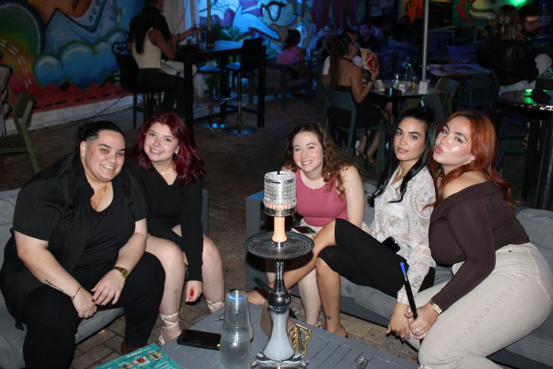 Group of friends on a Miami Vice Patio lounge couch with hookah at Grails Wynwood — covered patio bar with TVs