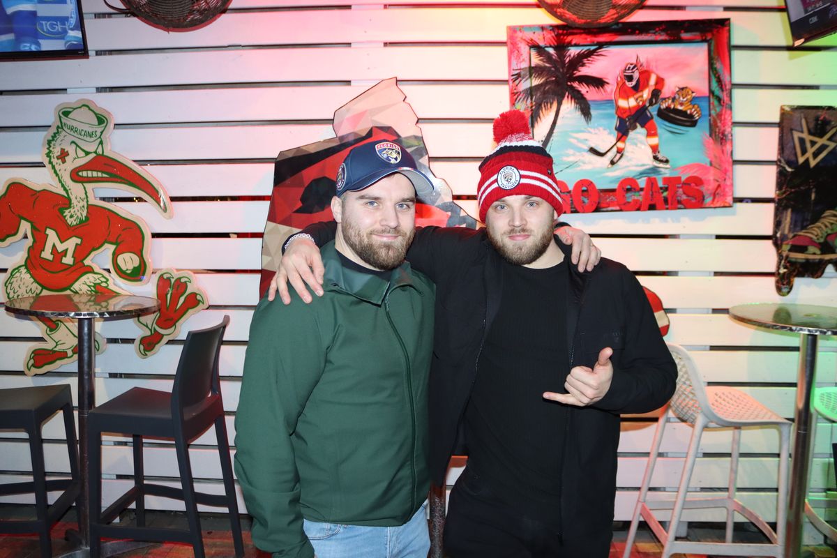 Two Florida Panthers fans posing arm-in-arm in red Panthers jerseys at Grails Miami during a Stanley Cup Playoffs watch party