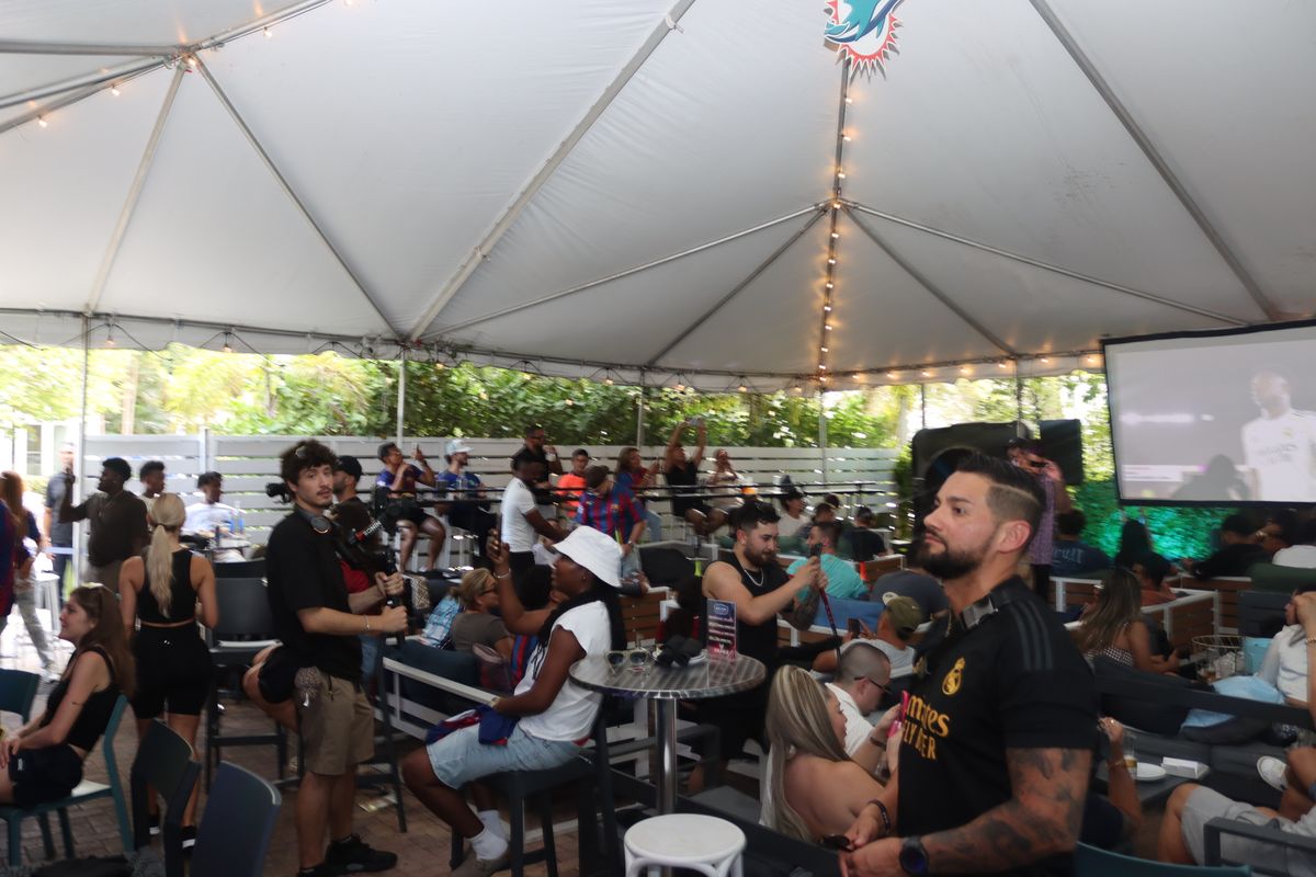 Crowd of soccer fans in Real Madrid and Barcelona jerseys watching a Champions League match on the Grails Miami patio