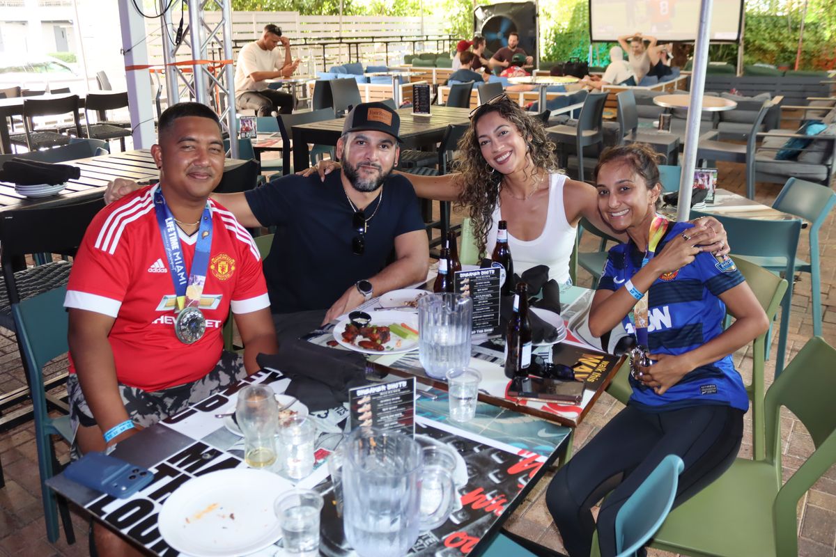 Friends in Manchester United and Chelsea jerseys posing at a patio table during a UEFA Europa League watch party at Grails Miami