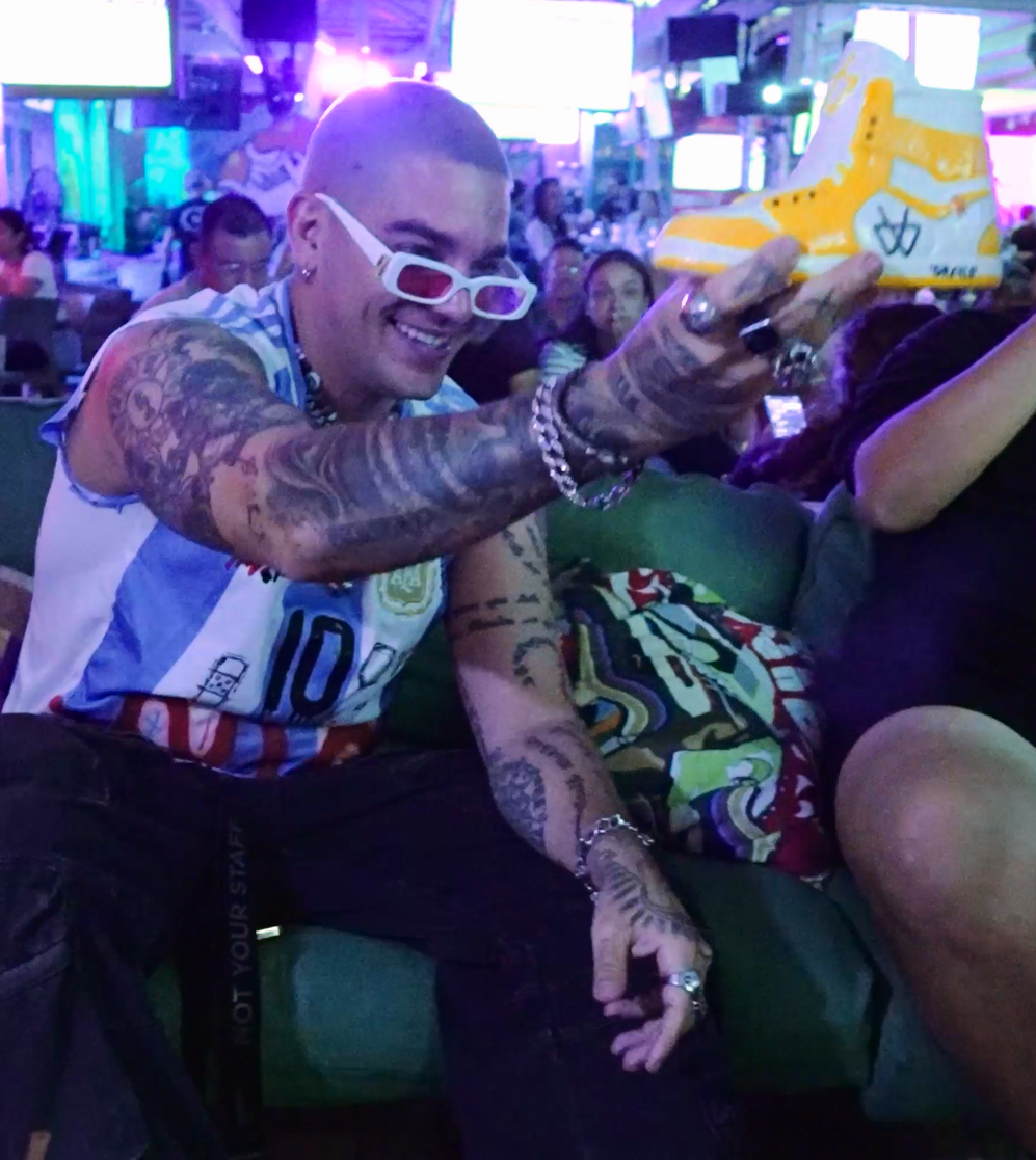 Argentina jersey fan holding up a yellow Grails sneaker cocktail at Grails Miami on World Cup night