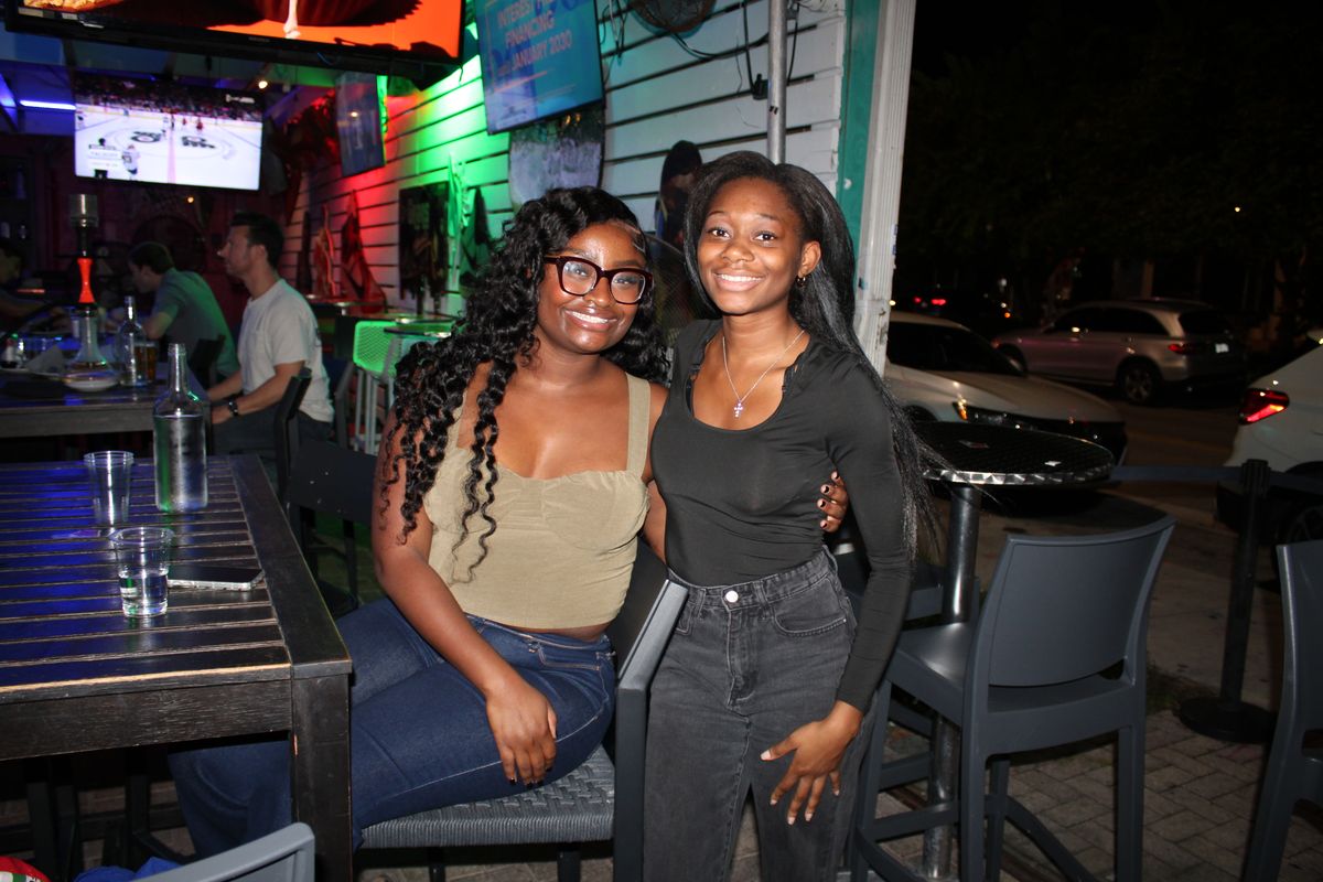 Two friends posing at the Grails Miami patio with a Stanley Cup Playoff hockey game on the TV behind them