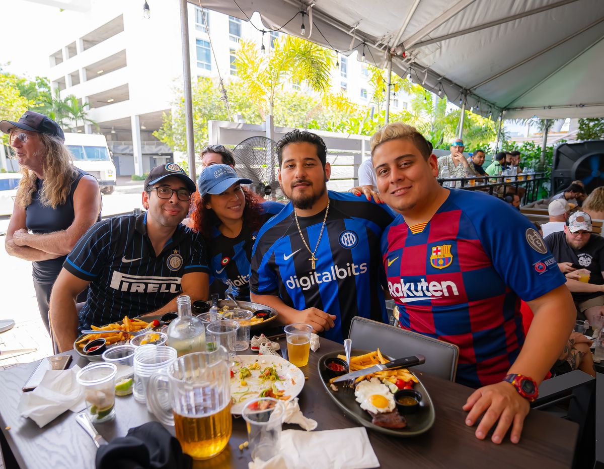 Inter Milan and Barcelona fans posing together at a Grails Miami patio table during a European football watch party