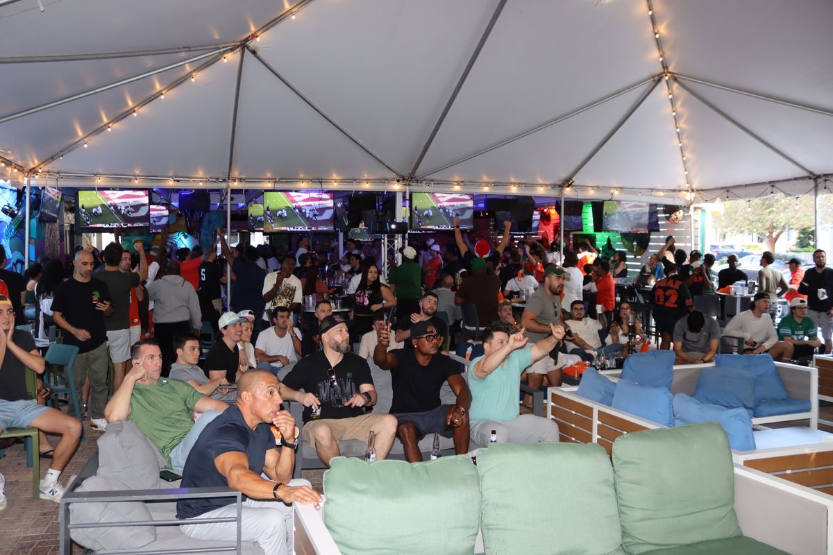College football fans watching a Playoff game on the giant projector under the Grails Miami tent
