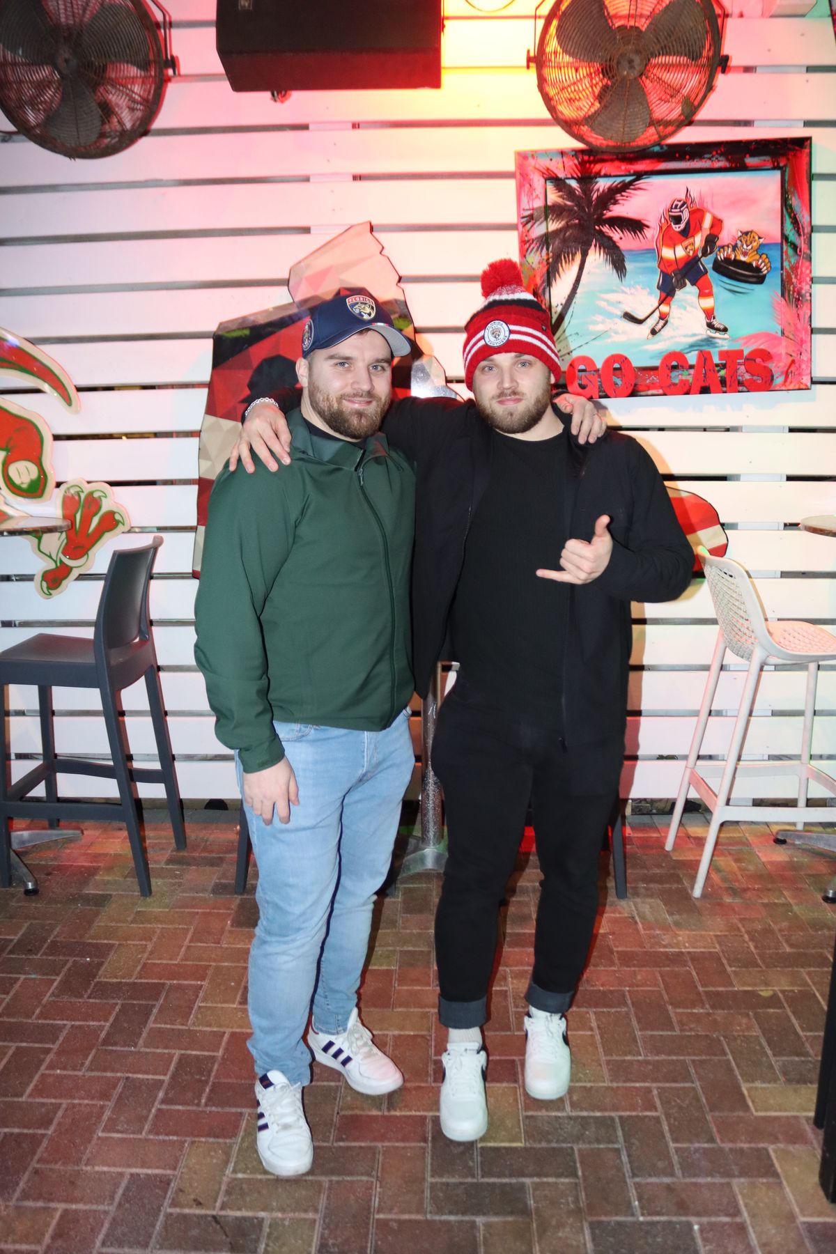 Two Florida Panthers fans posing in front of a Go Cats artwork wall during a Panthers watch party at Grails Miami