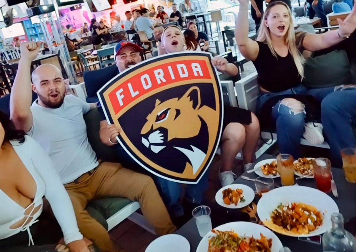 Group of Florida Panthers fans cheering around the Panthers shield logo at Grails Miami during a Stanley Cup Playoffs watch party