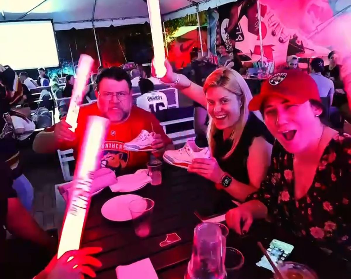 Florida Panthers fans in red team jerseys cheering with foam sticks and sneaker-shaped plates during a Panthers watch party at Grails Miami