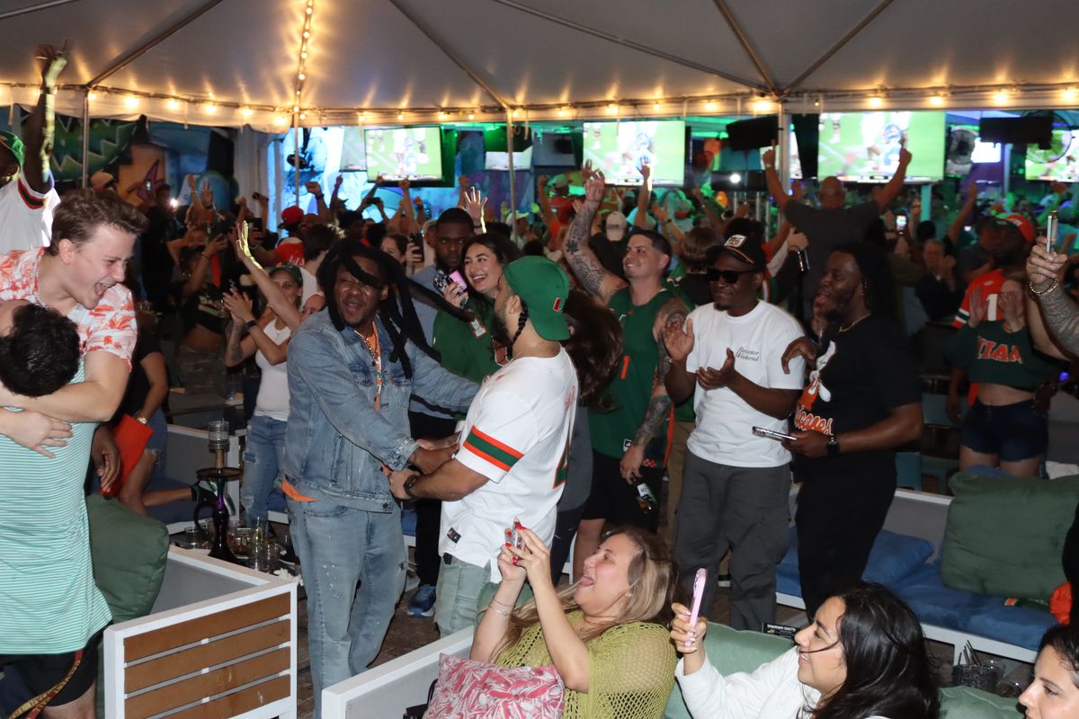 Miami Hurricanes fans celebrating a touchdown with hands in the air under the Grails Miami tent