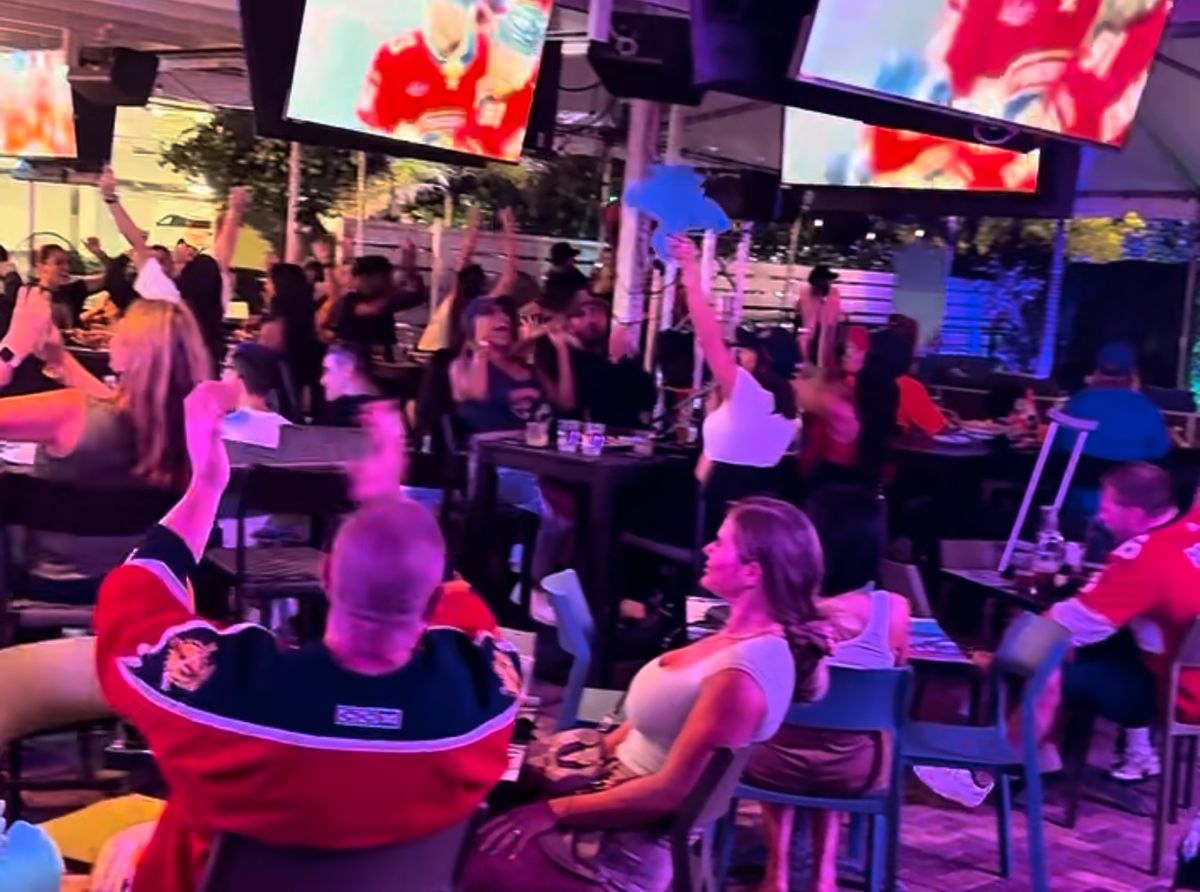 Florida Panthers fan in a red Panthers jersey raising arms while the Panthers play on overhead TVs at Grails Miami