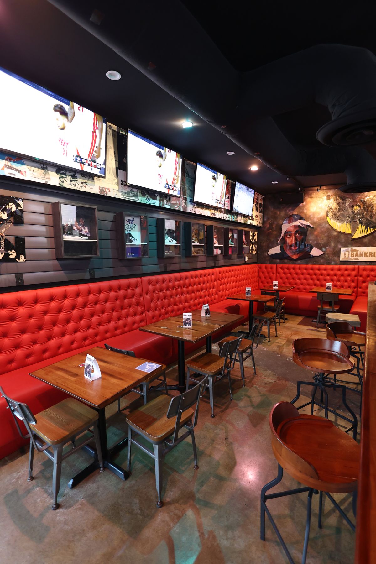 Wide interior view of the Sneaker Lounge at Grails Miami, with red tufted leather banquette seating beneath a row of flat-screen televisions and rare collectible sneakers displayed along the wall behind.
