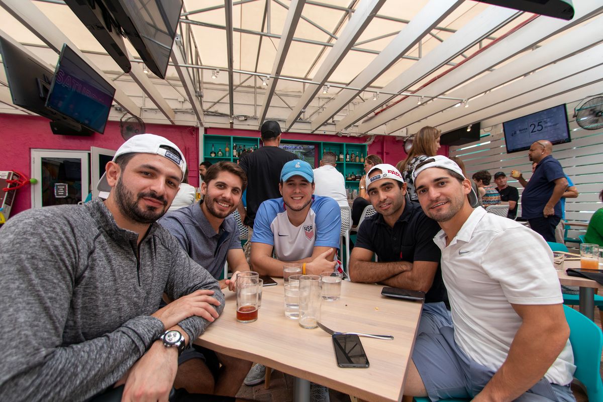 Group of five friends with one fan in a USA soccer jersey at the Grails Miami patio during a Concacaf Gold Cup watch party
