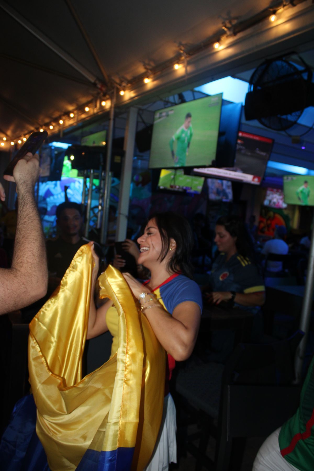 Woman wrapped in a Colombian national flag laughing during a Copa Libertadores watch party on the Grails Miami patio