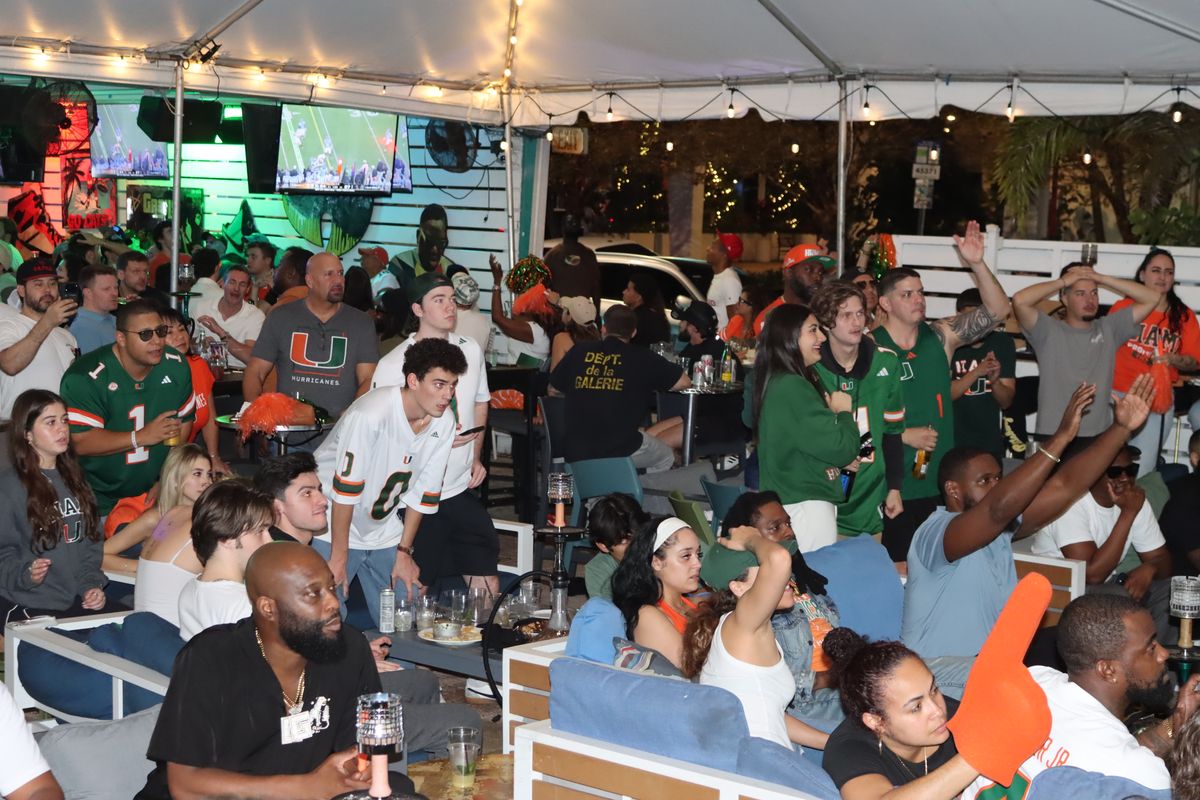 Crowd in Miami Hurricanes jerseys watching a College Football Playoff game on the patio at Grails Miami
