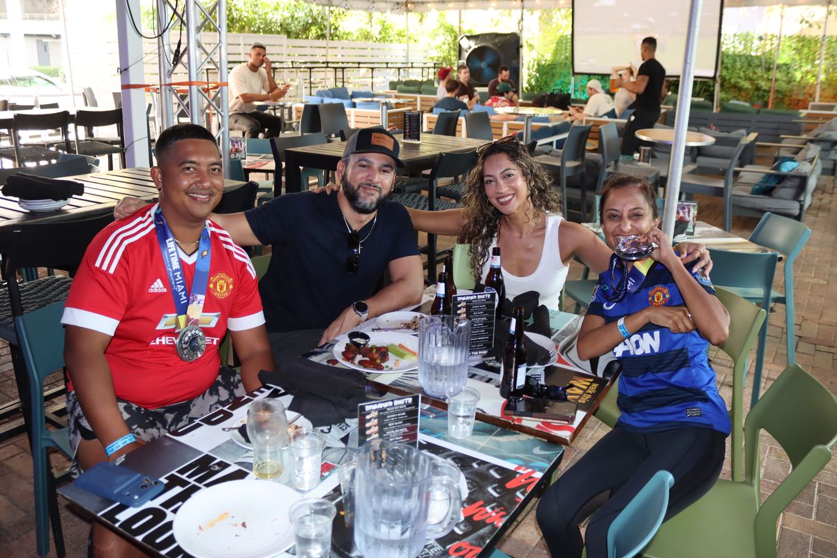 Group of Manchester United fans in red jerseys posing at a Grails Miami patio table during a Premier League watch party in Miami