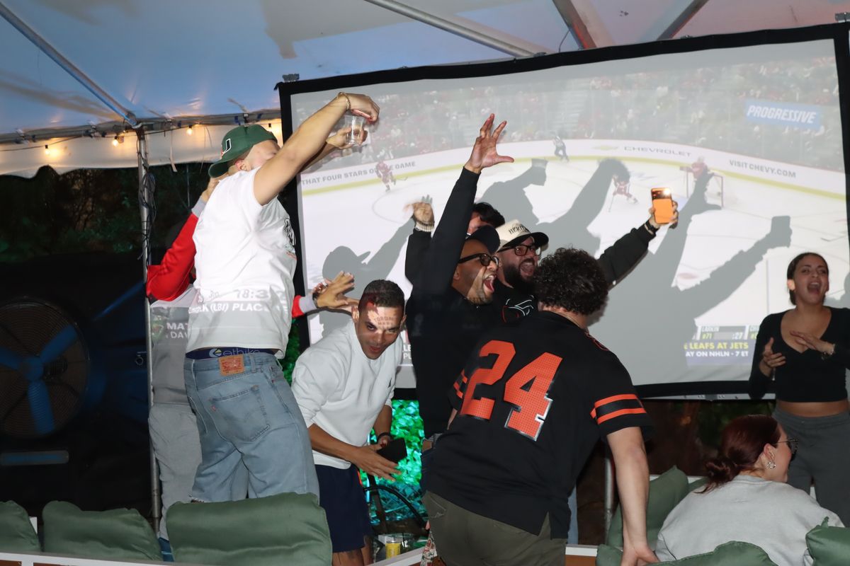 Hockey fans celebrating with arms up under the Grails Miami tent during a Stanley Cup Playoff watch party