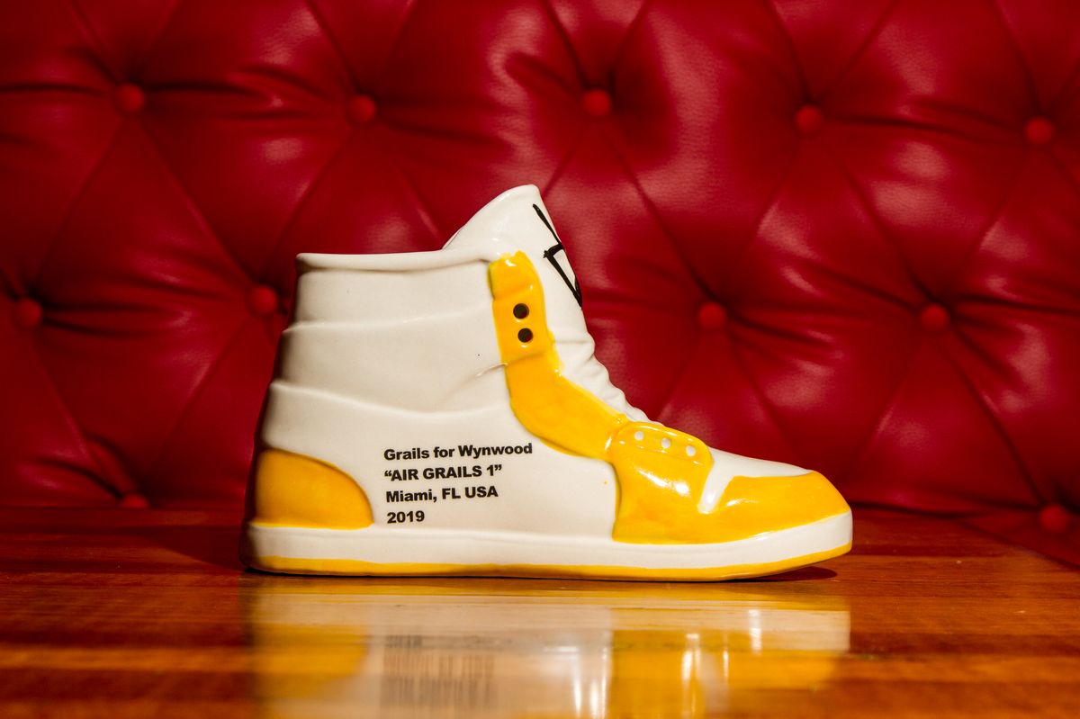 Air Grails 1 Yellow ceramic sneaker cocktail cup, white with yellow Jordan 1 panel detailing on a wooden bar at Grails Miami