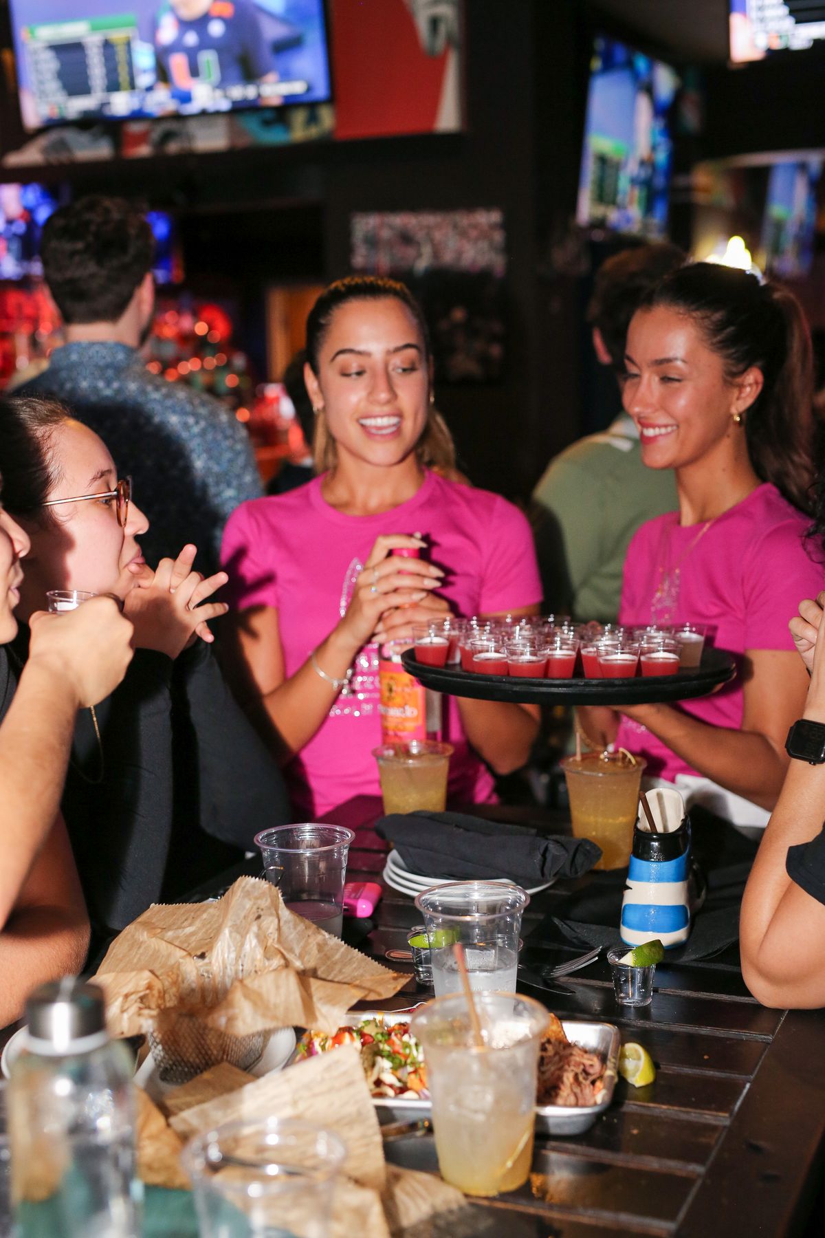 Grails servers in pink shirts presenting a tray of shots during happy hour at Grails Miami in Wynwood