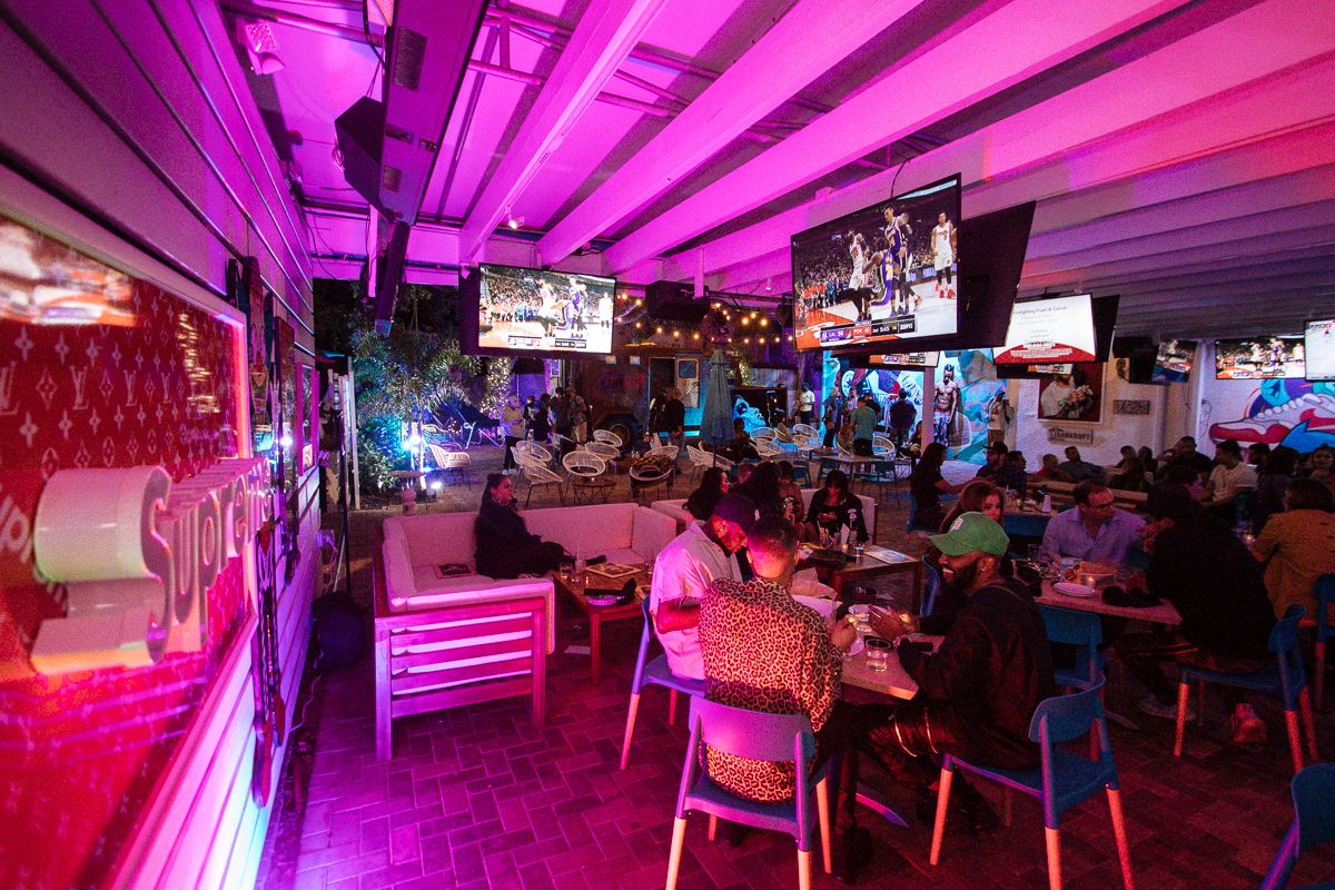 The covered Miami Vice Patio at Grails Miami filled with guests dining under pink lighting and overhead TVs.