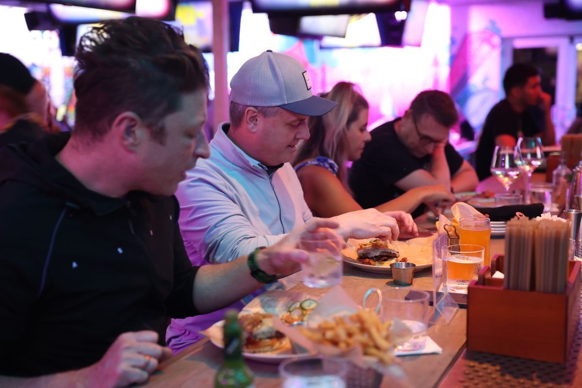 Guest in a grey trucker cap eating a burger at the Grails Miami bar counter during brunch.