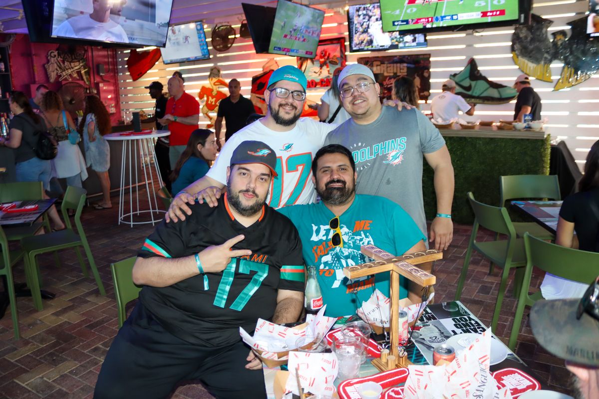 Group of Miami Dolphins fans in #17 and Dolphins jerseys posing at a Grails Miami patio table on a Dolphins game day
