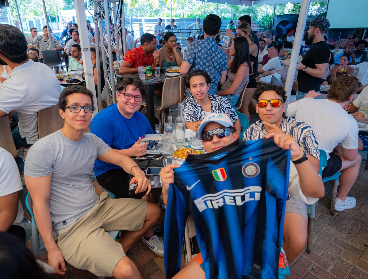 Friends holding up an Inter Milan jersey at a Grails Miami patio table during a Serie A watch party in Miami