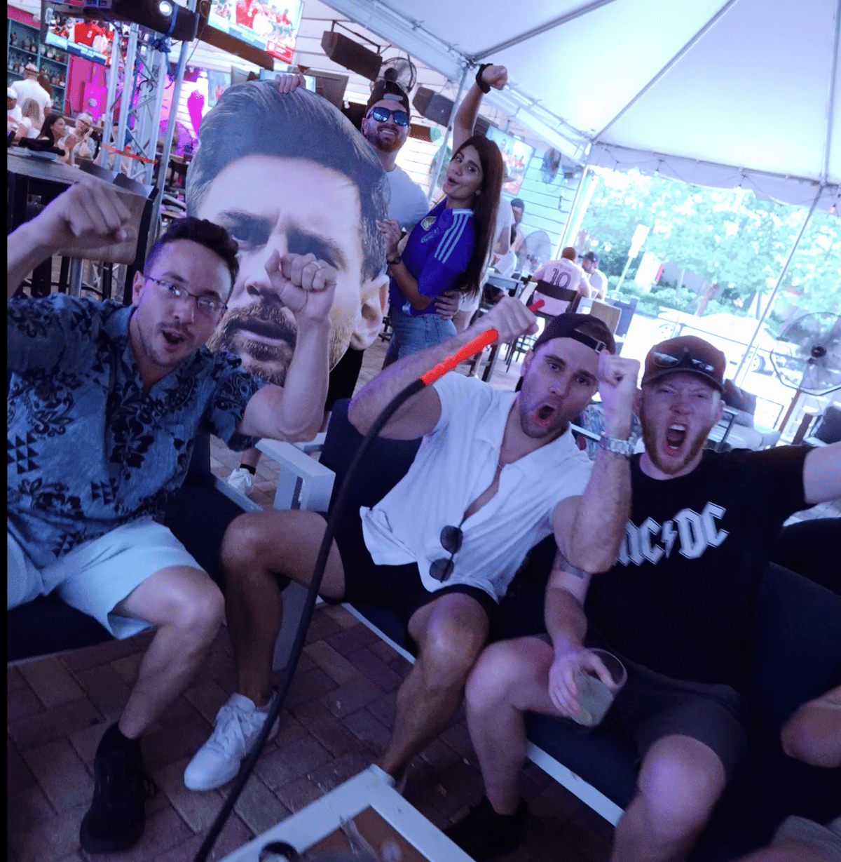 Group of Inter Miami fans cheering with a giant Lionel Messi face cutout during a watch party at Grails