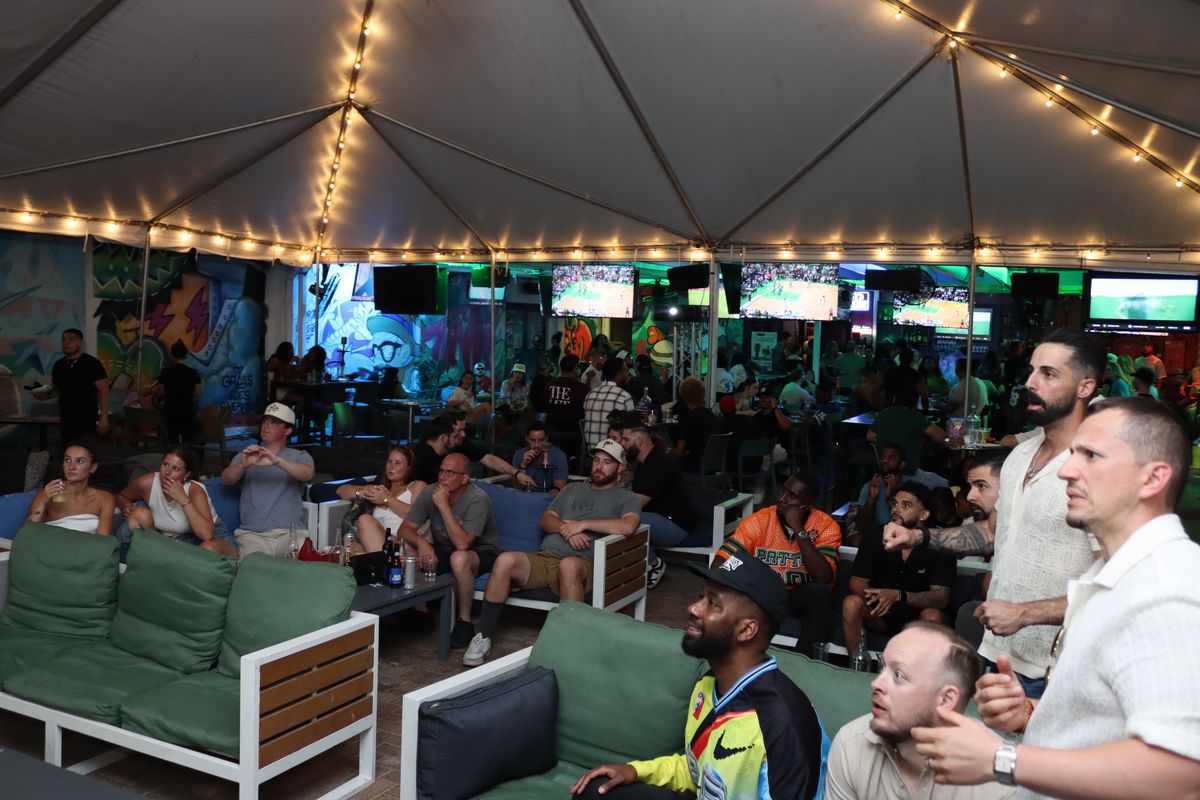Crowd at Grails Miami's tented Yard with basketball on the giant projector screen during a WNBA Finals night