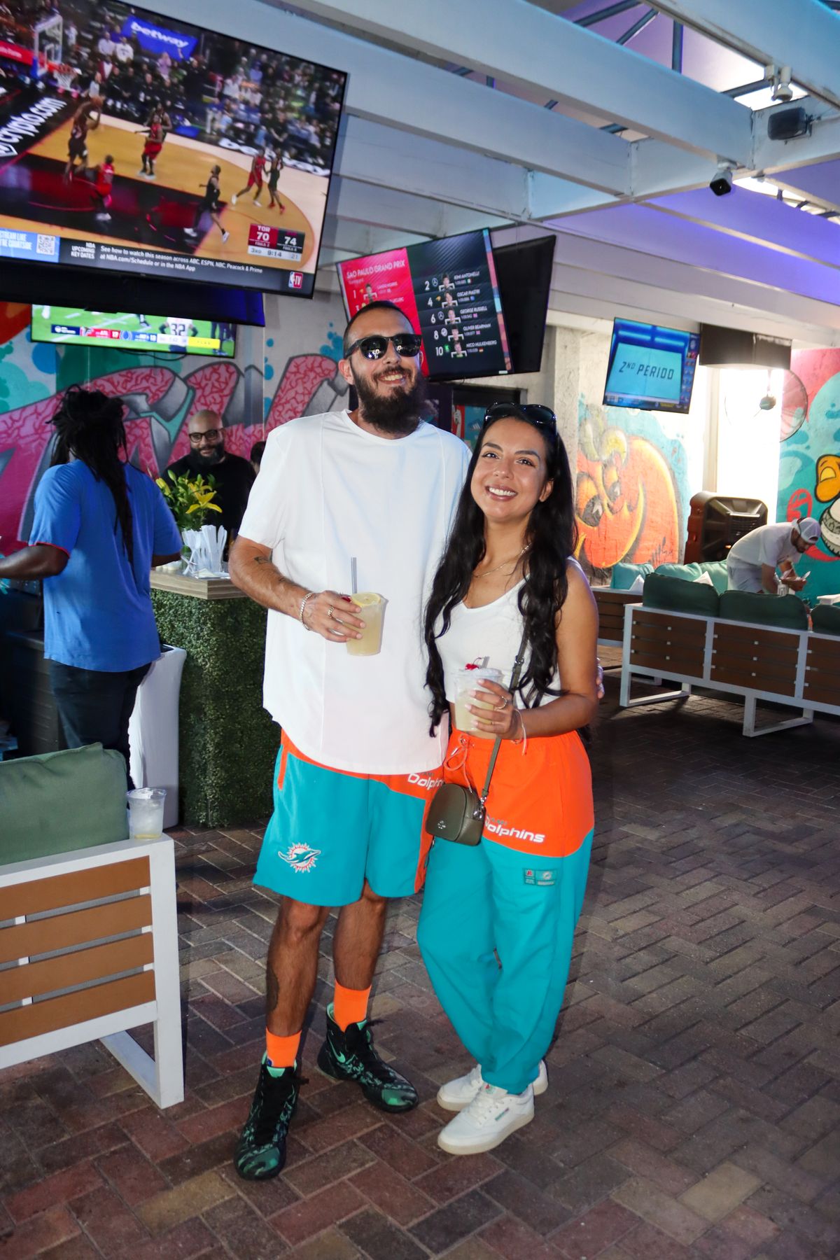Miami Dolphins fan couple in matching aqua Dolphins gear on the Grails Miami patio under the bar TVs