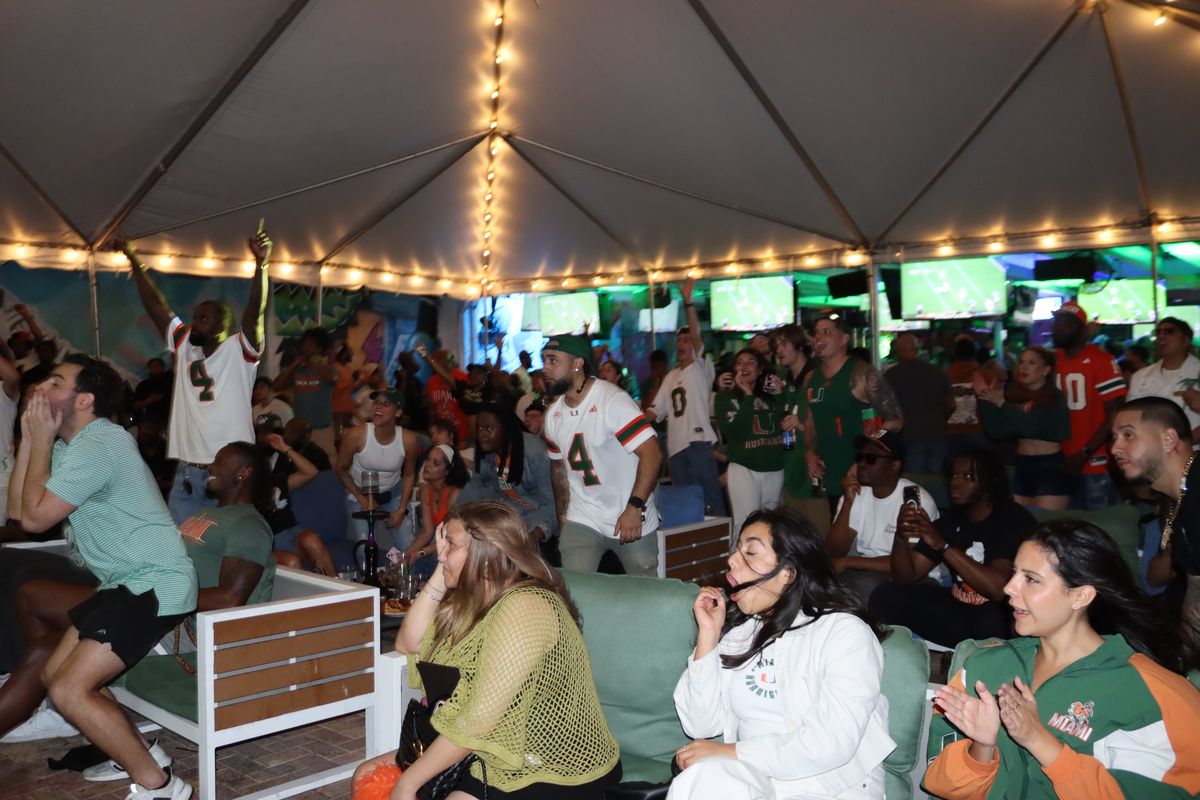 Miami Hurricanes fans in #4 and #10 jerseys reacting to a play under the Yard tent at Grails Miami