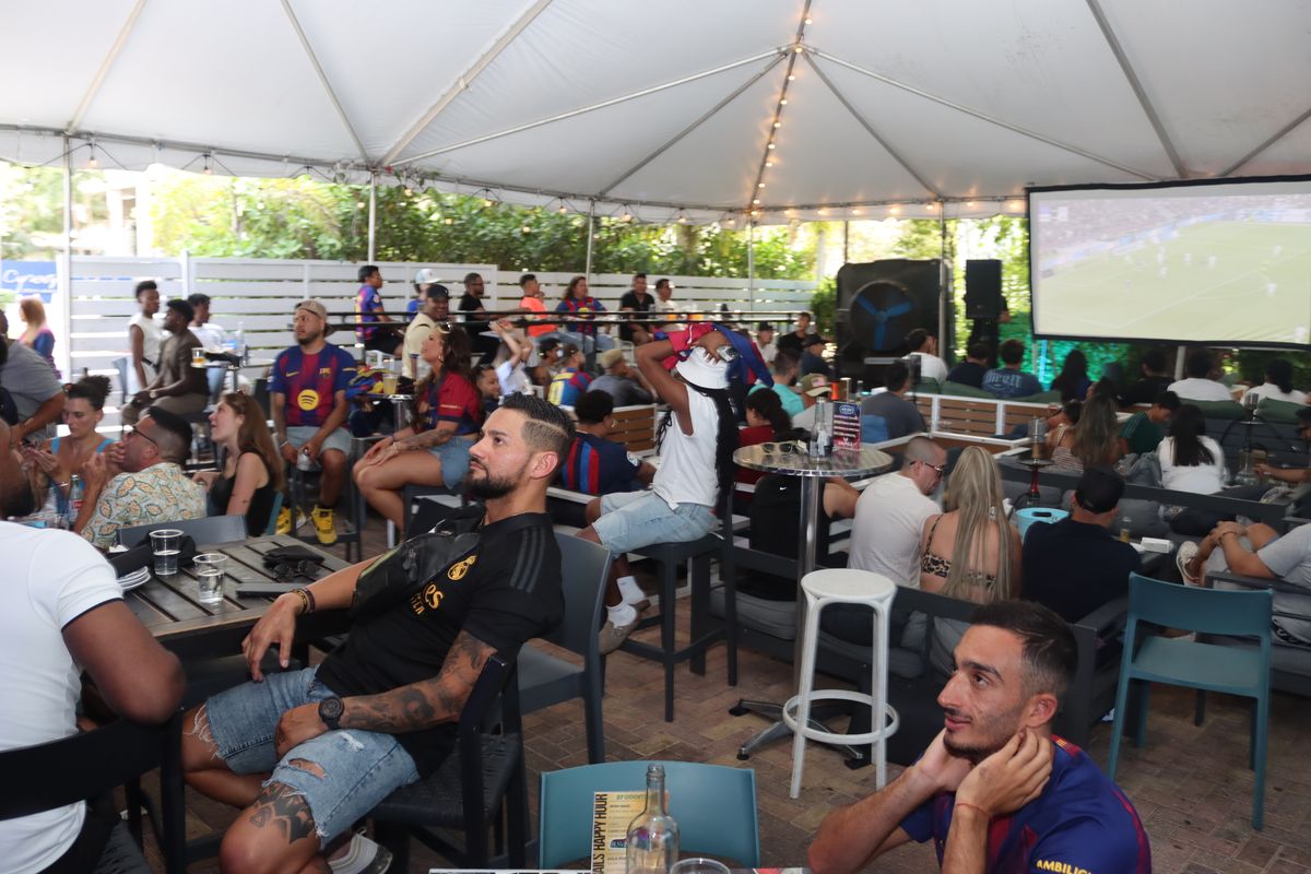 Soccer fans in Barcelona and Real Madrid jerseys watching a Champions League match from the patio bar at Grails Miami
