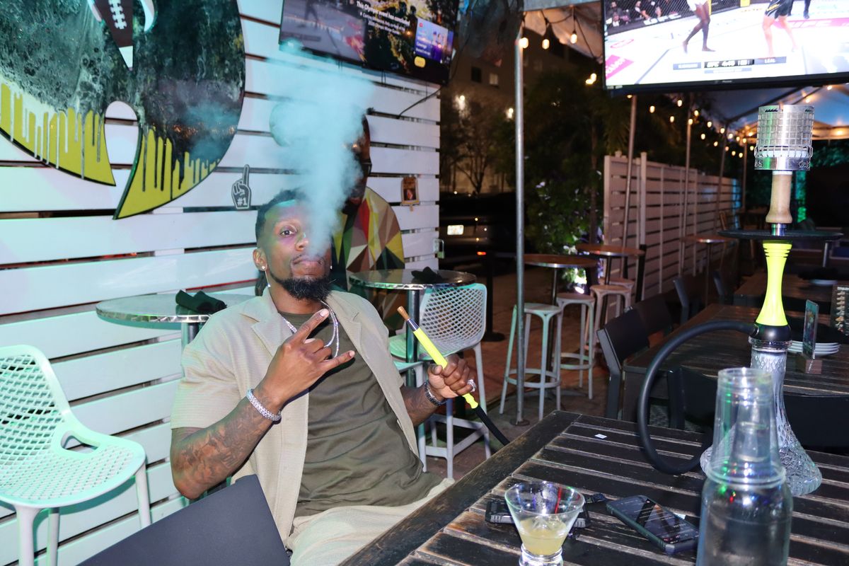 Guest at Grails Miami exhaling hookah smoke on the covered patio under the sports TV — the best Wynwood hookah bar in Miami, located two blocks from Wynwood Walls at 2800 N Miami Ave.