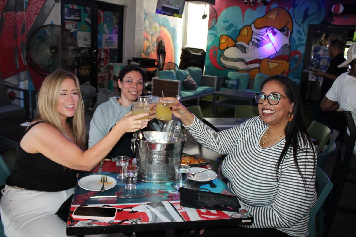 Three friends toasting happy hour cocktails at Grails Miami in Wynwood