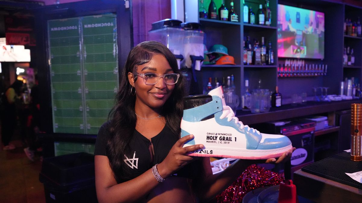 A smiling Grails Miami bartender holding the signature Holy Grail 1 sneaker-shaped cocktail vessel behind the bar