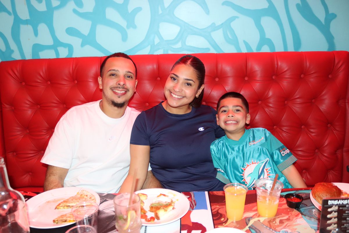Family of three at a red booth at Grails Miami with the son in a Miami Dolphins #1 jersey