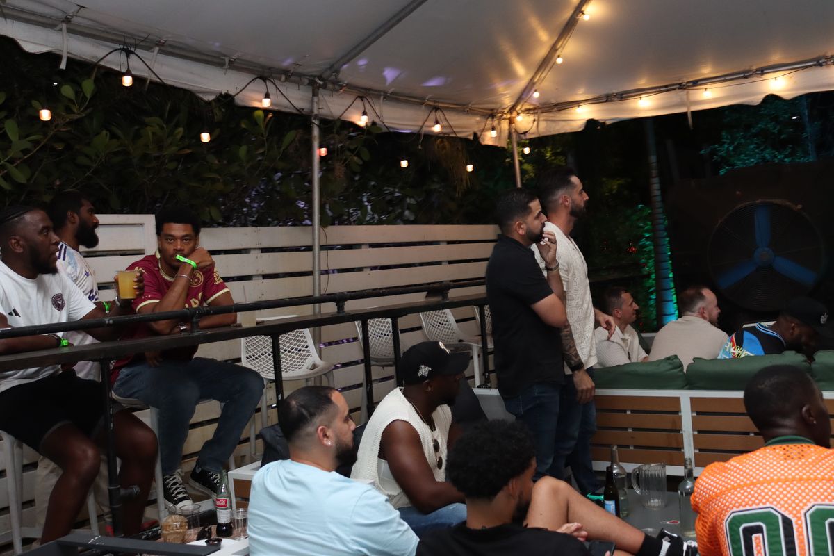 Group of soccer-jersey-clad fans watching an Inter Miami match on the covered Grails Miami patio