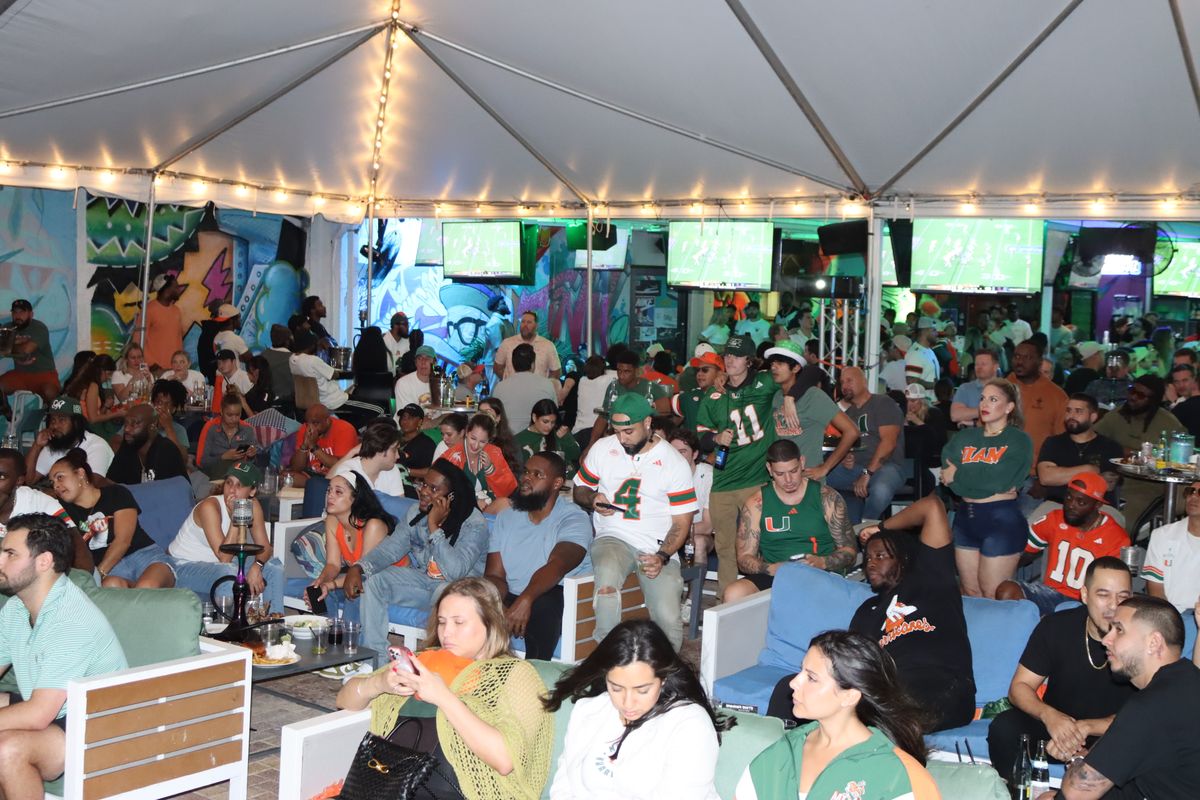 Miami Hurricanes fans in MIAMI #84 jerseys watching the Hurricanes on the giant projector under the Grails Miami tent