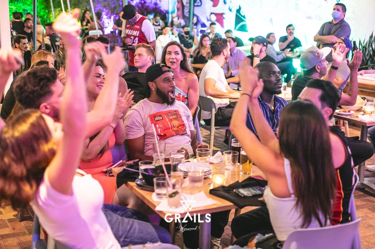 Miami Heat fans cheering and clapping around a table at Grails Miami during a Heat watch party