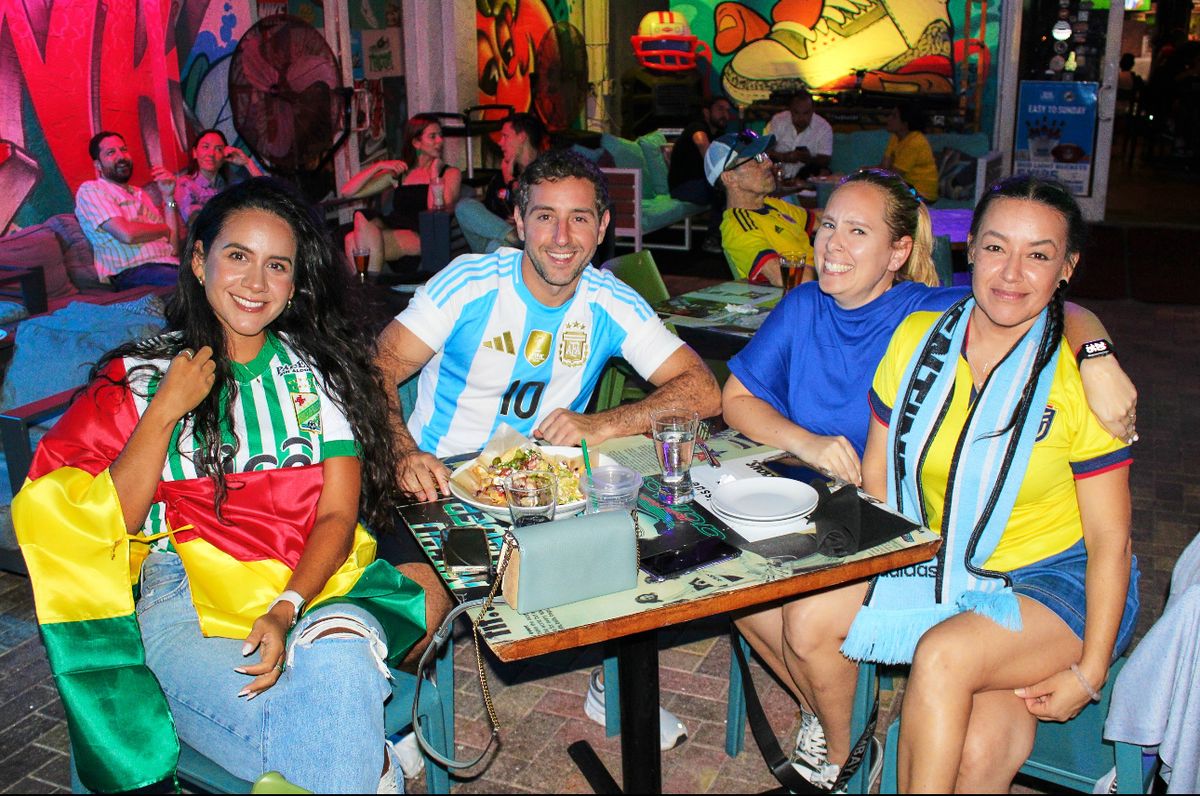 Four soccer fans in South American national jerseys posing at a Grails Miami patio table during a Copa Libertadores watch party