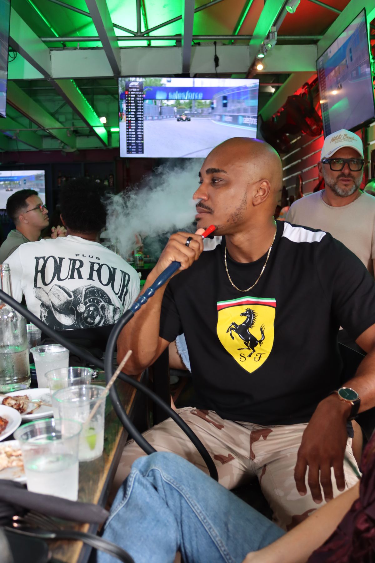 Ferrari-shirt F1 fan smoking hookah at Grails Miami while watching the Miami Grand Prix on the patio TV — Formula 1 hookah watch party in Miami