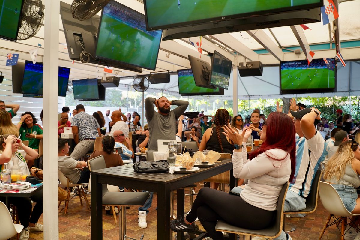 Soccer fans on the Grails Miami covered patio watching World Cup matches across multiple overhead TVs