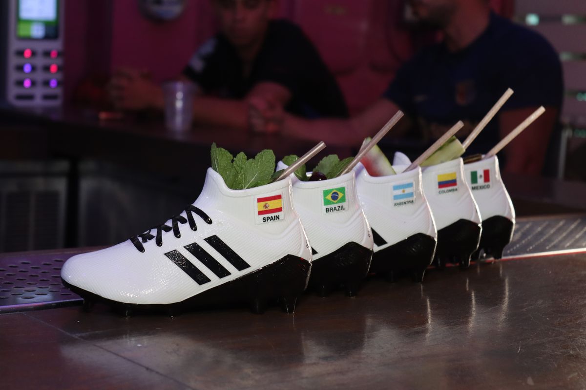 Row of five Grails Cleats ceramic World Cup cocktails on the bar at Grails Miami, Spain, Brazil, Argentina, Colombia and Mexico flag stickers visible on the heels