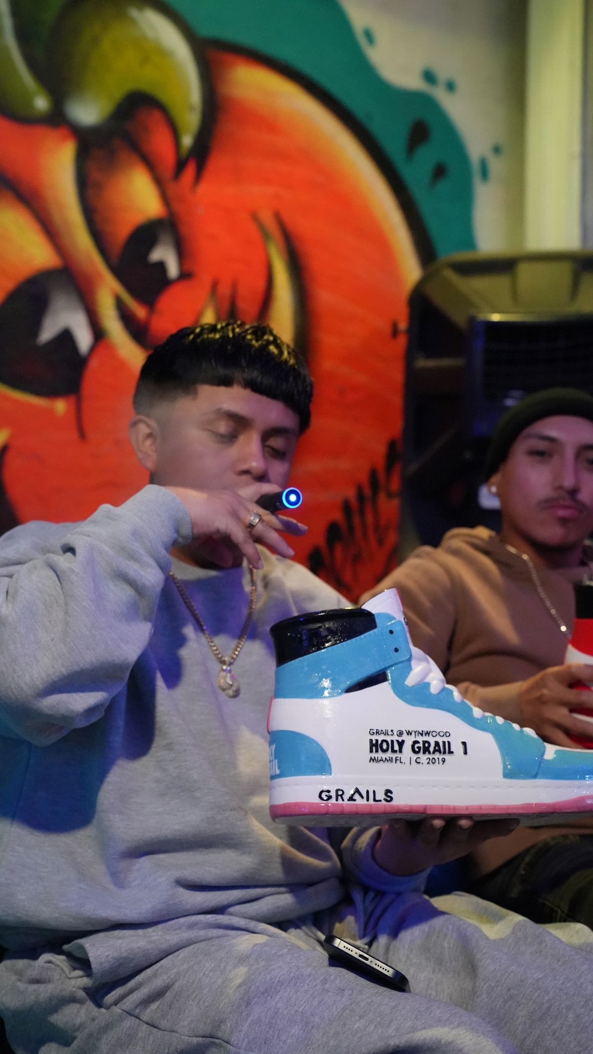 Guest at Grails Miami holding up the red and white Holy Grail 1 ceramic sneaker cocktail cup, the famous Wynwood drink-in-a-shoe cocktail served at 2800 N Miami Ave.