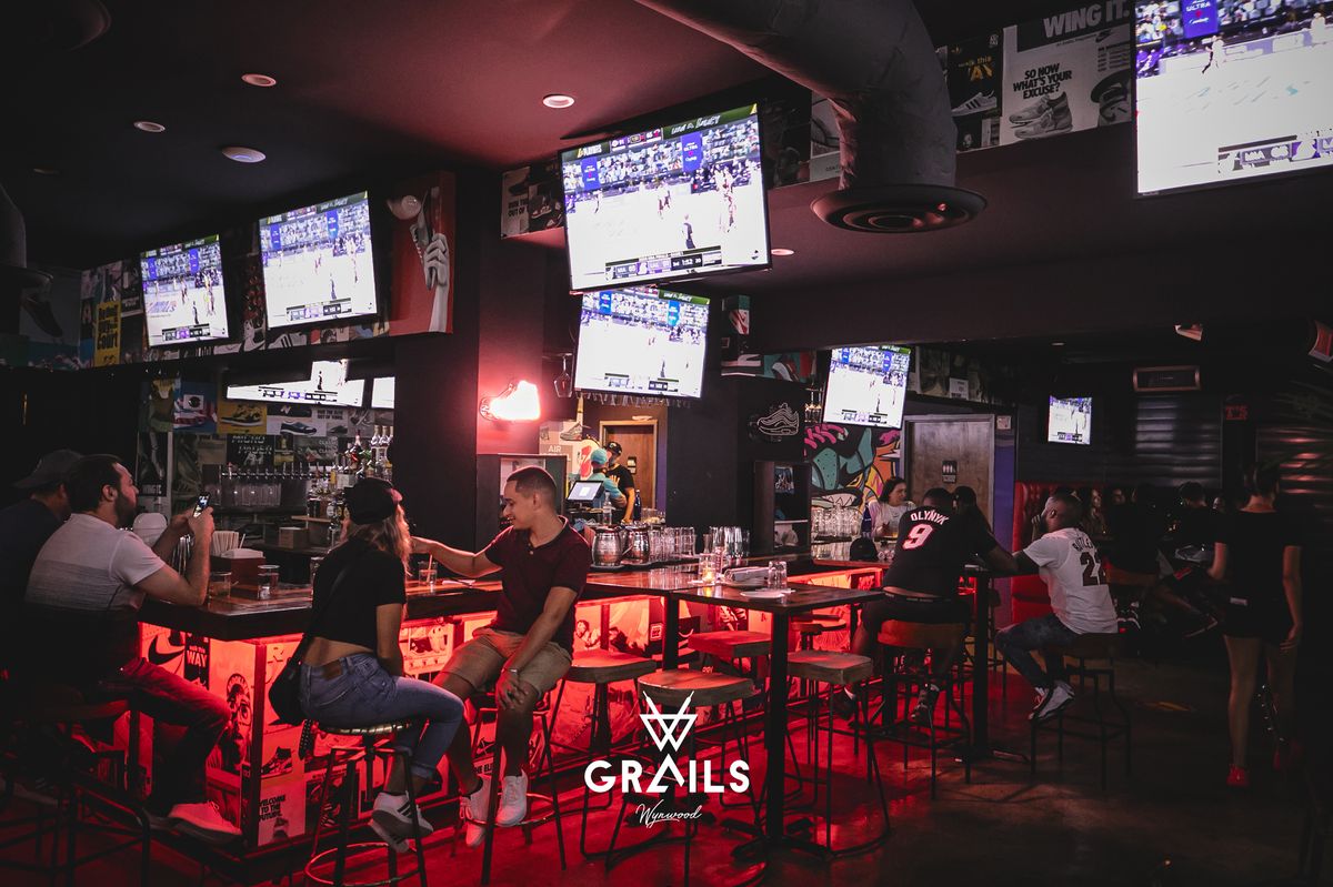 Wide interior of Grails Miami with patrons watching the NBA Playoffs on overhead TVs at the Miami Heat watch party bar