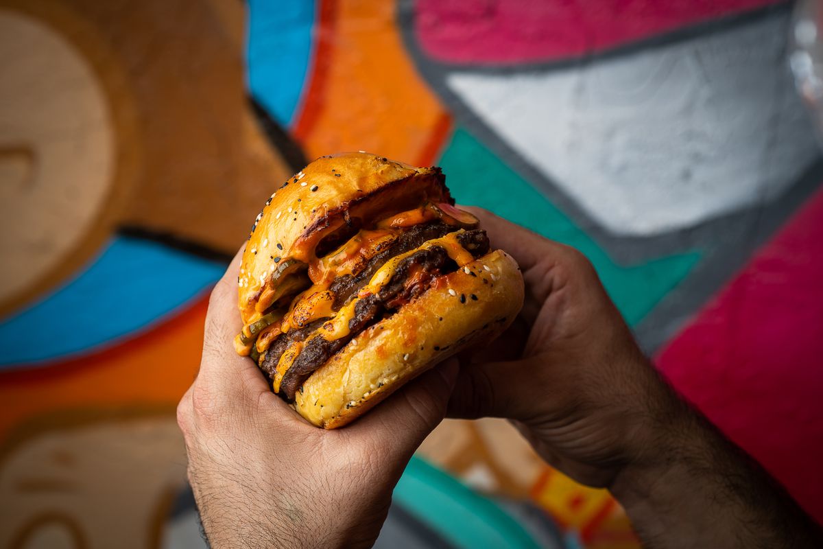 Double smash burger held in hands against the Wynwood mural at Grails Miami brunch.