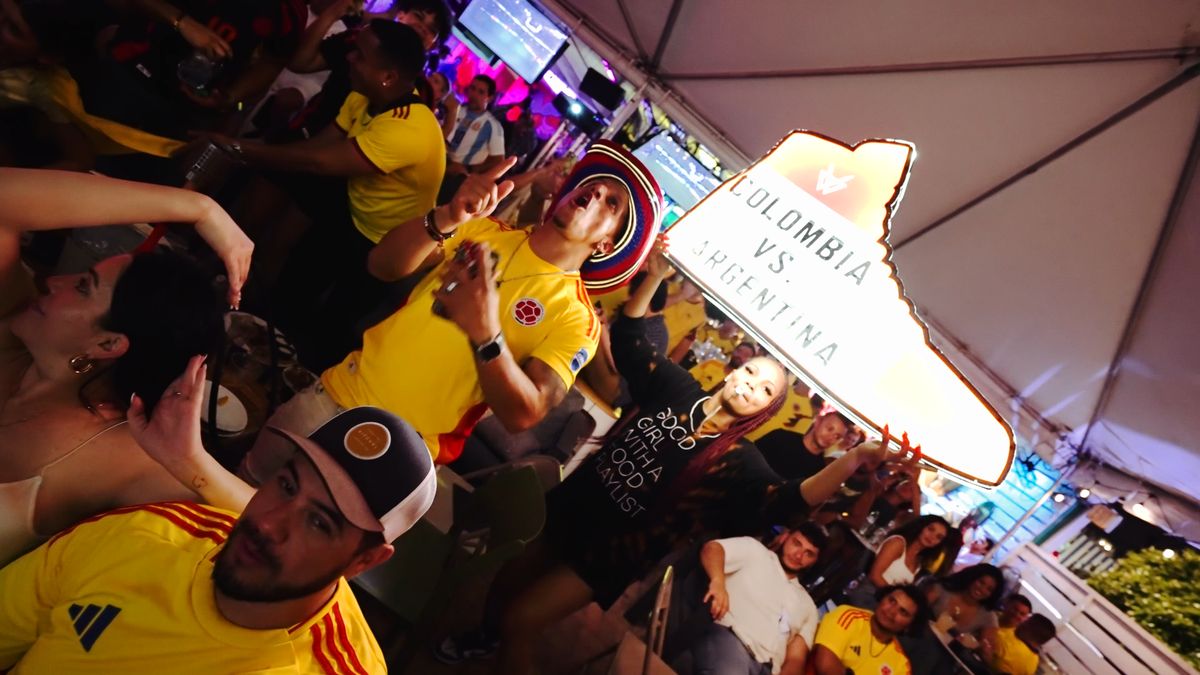 Colombia fans cheering beside an illuminated Colombia vs Argentina sneaker sign at Grails Miami, Miami's World Cup watch party bar