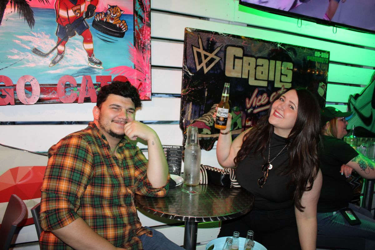 Smiling couple at a Grails Miami table with a Corona beer raised in front of a Florida Panthers mural