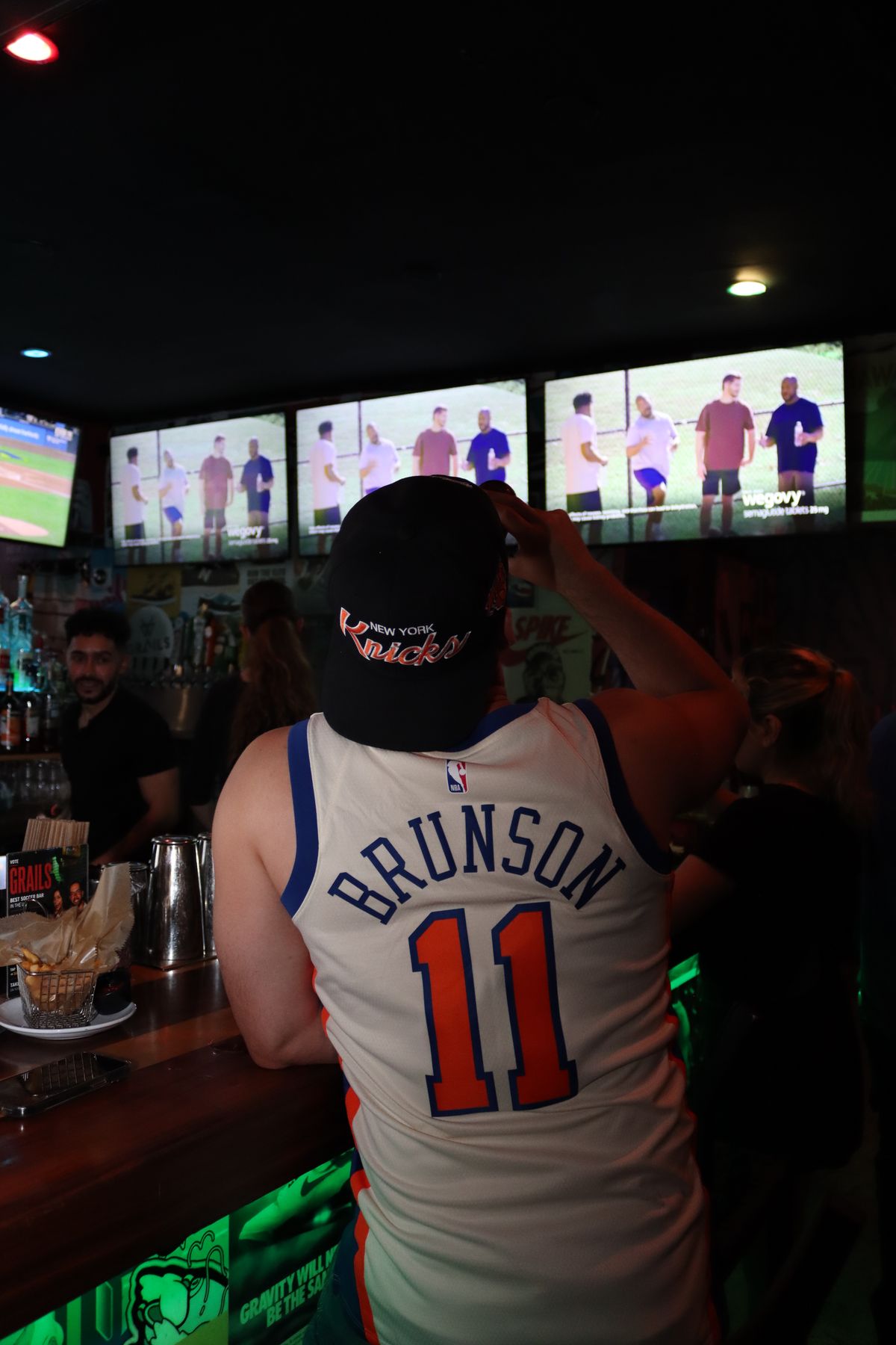 Knicks fan in a Brunson jersey watching the NBA at a Grails Miami table