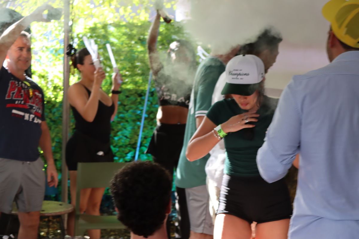 Philadelphia Eagles and New York Jets fans celebrating with foam sticks and smoke on the Grails Miami patio during an NFL watch party