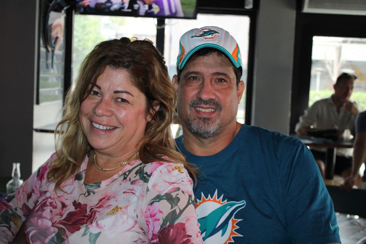 Smiling couple at Grails Miami with the husband in a Miami Dolphins T-shirt and Dolphins cap