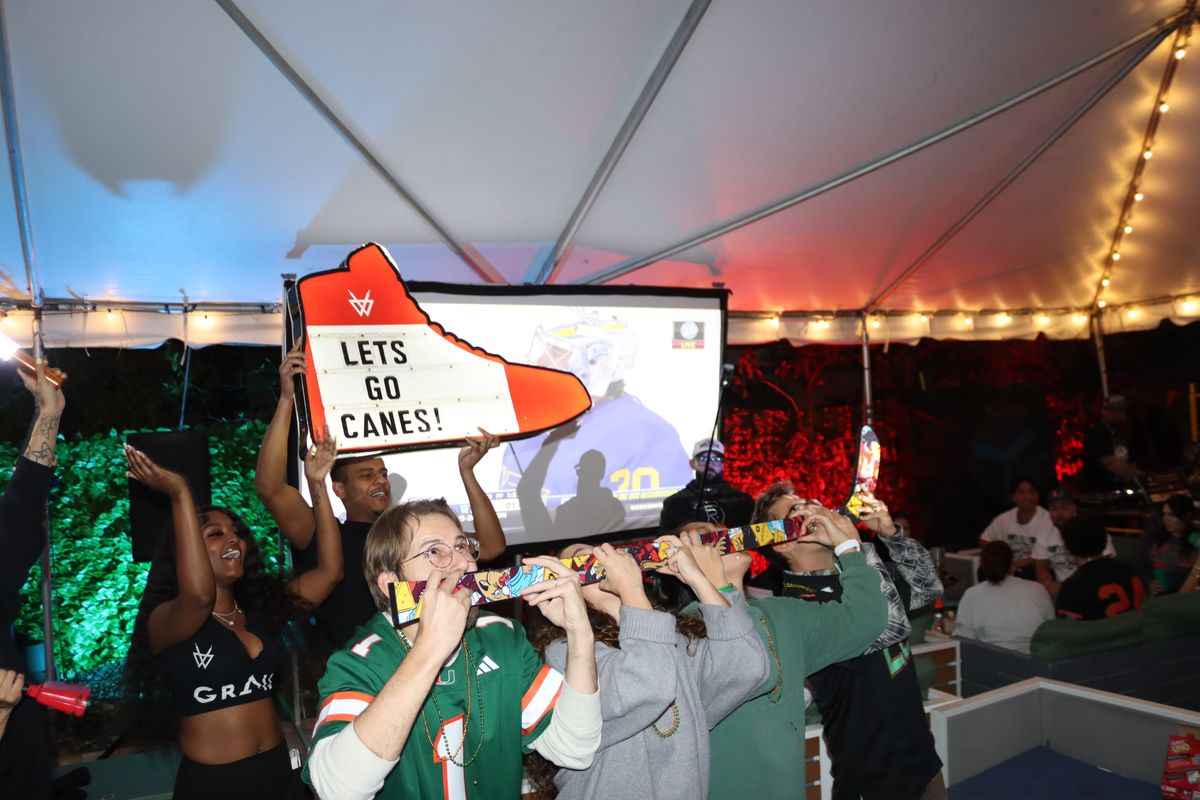 Miami Hurricanes fans drinking from a Hurricanes-branded shot-ski next to a Let's Go Canes sneaker sign at Grails Miami